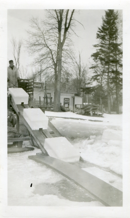 Photo of blocks of ice on an elevated conveyor belt with a man, John Ferguson, standing at the top of the elevator