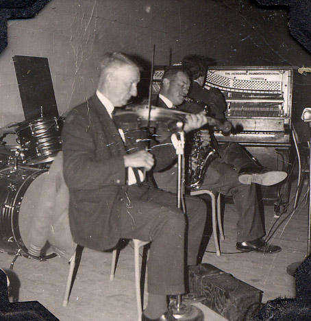 two gentlemen seated on stage playing violins