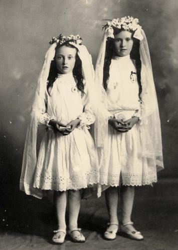 Two girls in white dresses and veils, black and white photo for confirmation. There are garlands in their hair.