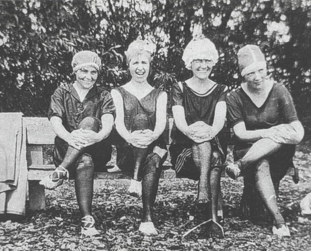 black and white photo of 4 ladies in bathing caps and old fashioned swim suits sitting on a bench