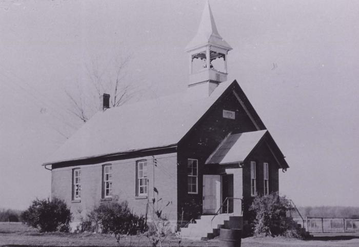 black and white photo of brick one room school house with bell tower