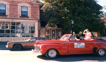 Image of the Cookstown Fair Queen riding in a vintage red car in 1990